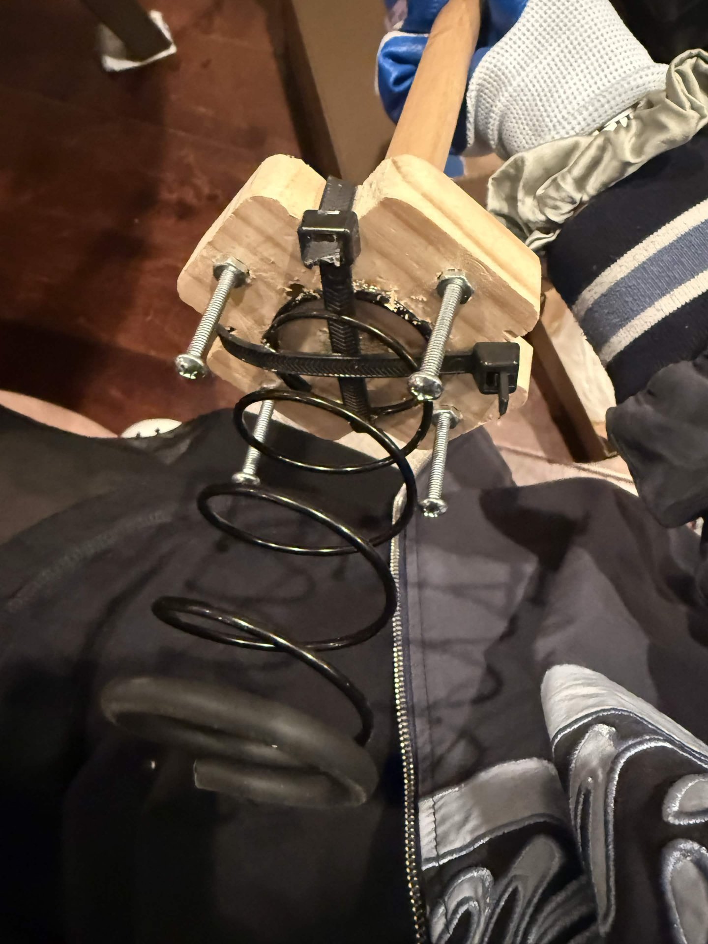 Underside of the wooden plunger showing a spring, screws, and cable ties